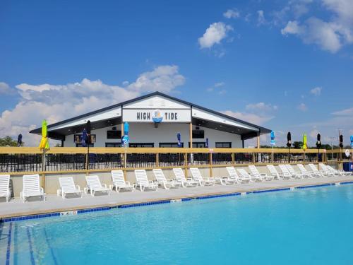 A swimming pool with lounge chairs in front of a building labeled "High Tide" under a blue sky with clouds.