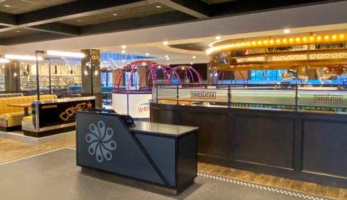 Interior of a modern restaurant featuring a counter, seating area, and a carousel-themed dessert display.