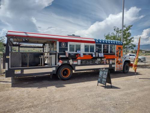 A colorful food truck with an American flag design parked outdoors, featuring a menu board and various stickers.