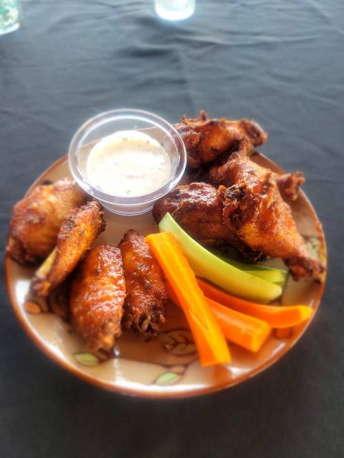 A plate of crispy chicken wings with celery, carrots, and a small cup of dipping sauce.
