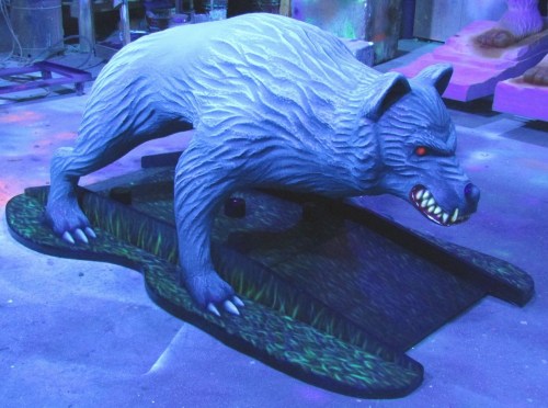 A large, stylized blue bear sculpture with red eyes, positioned on a grassy base in a dimly lit space.