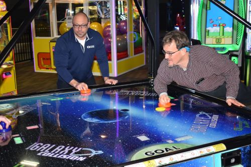 Two men play a game of air hockey in an arcade, focused on the colorful game surface featuring a space theme.