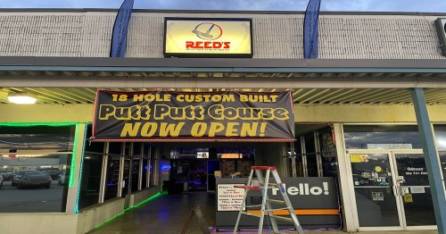 Sign for Reed's Entertainment featuring a banner that reads "18 Hole Custom Built Putt Putt Course NOW OPEN!"