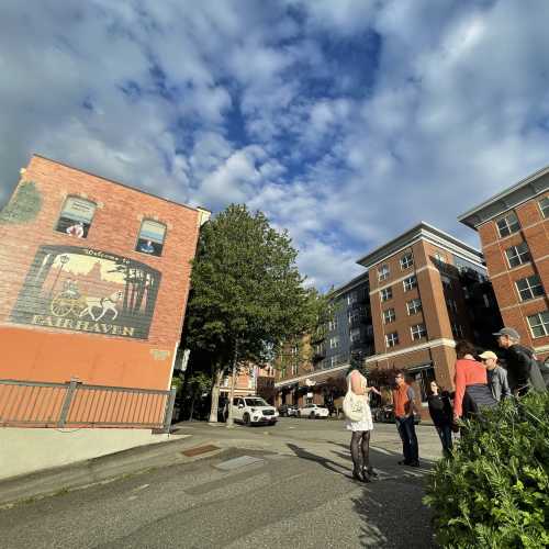 A mural on a brick wall in Fairhaven, with people gathered on the street under a partly cloudy sky.