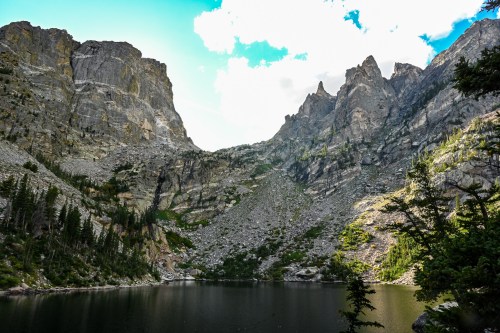 A serene mountain landscape featuring towering cliffs surrounding a calm lake under a bright blue sky.