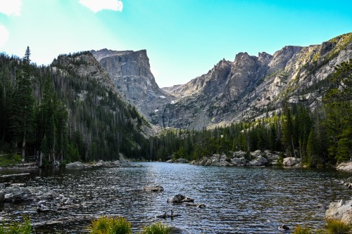 A serene mountain lake surrounded by towering cliffs and lush green trees under a clear blue sky.