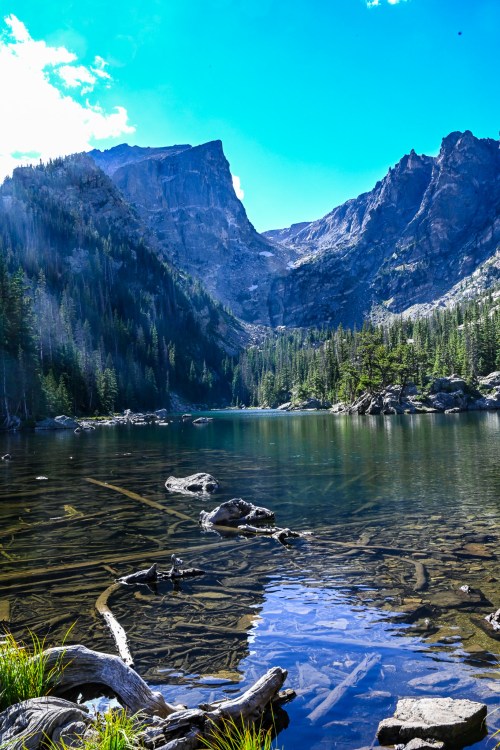A serene mountain lake surrounded by tall trees and rocky cliffs under a bright blue sky.