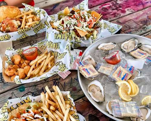 A spread of fried seafood, fries, nachos with toppings, and a platter of oysters with lemon on a colorful table.
