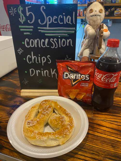 A plate with a pretzel, a bag of Doritos, and a bottle of Coca-Cola next to a sign advertising a $5 special.