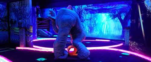 A glowing mini-golf course featuring a large elephant sculpture amidst vibrant neon lights and a forest backdrop.