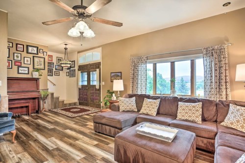 Cozy living room with a sectional sofa, decorative pillows, a piano, and a large window overlooking greenery.