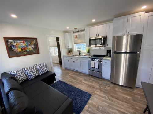 Modern kitchen with stainless steel appliances, white cabinets, and a cozy living area featuring a black sofa and blue rug.