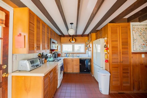 Cozy kitchen with wooden cabinets, white appliances, and exposed beams, featuring a window and tiled floor.