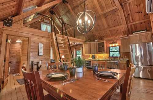 Cozy wooden cabin interior with a dining table, kitchen, and lofted area, featuring warm lighting and rustic decor.