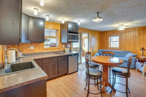 Cozy kitchen with dark cabinets, a round table, and a living area featuring a blue couch and wooden walls.