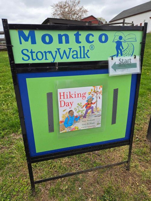 Sign for Montco StoryWalk featuring "Hiking Day" book cover, with a "Start" marker on a green and blue background.