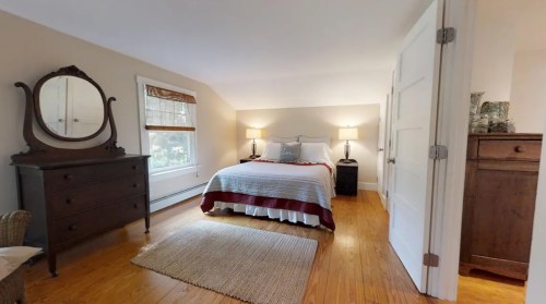 Cozy bedroom with a bed, two lamps, a dresser, and a rug, featuring warm wood floors and natural light.