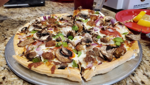 A pizza topped with mushrooms, green peppers, onions, and sausage, served on a silver platter.