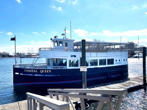 A blue and white boat named "Coastal Queen" docked at a marina on a sunny day.