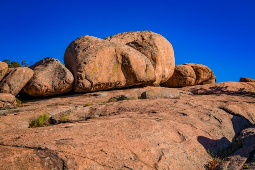 Large, smooth boulders atop a rocky surface under a clear blue sky.