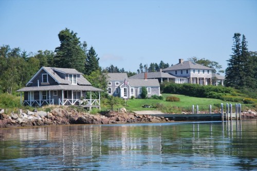 A scenic view of two houses by the water, surrounded by trees and a calm shoreline.