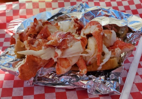 A lobster roll topped with chunks of lobster meat, served on a foil-lined tray with a red and white checkered background.