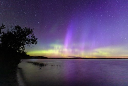 A serene lake at night, illuminated by vibrant purple and green auroras under a starry sky.