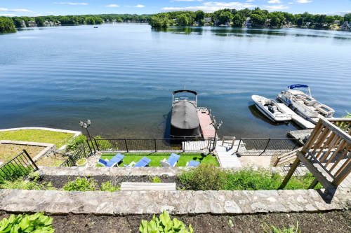 A serene lake view with boats docked, steps leading down to a grassy area, and a clear blue sky above.