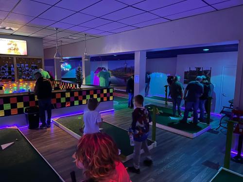 A dimly lit mini-golf venue with colorful decor, people playing, and neon lights creating a vibrant atmosphere.