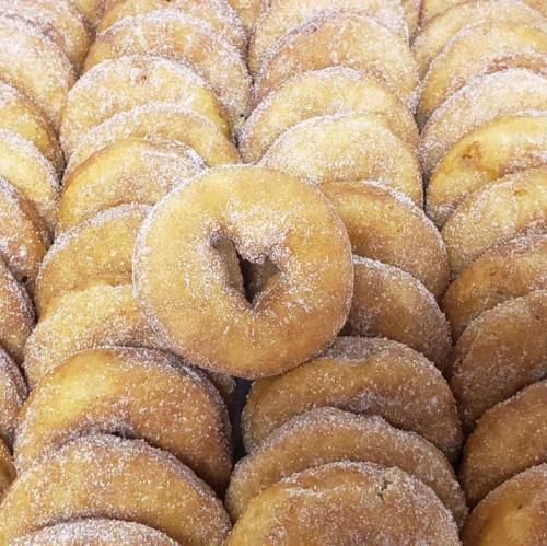 A close-up of a large batch of sugar-coated donuts arranged in a neat pattern, with one donut slightly off-center.