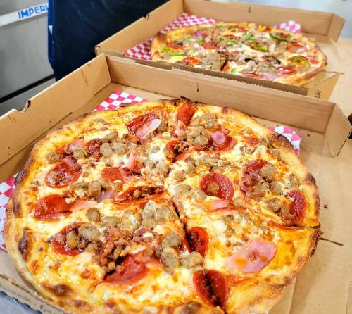 Two pizzas in cardboard boxes: one topped with pepperoni and sausage, the other with various vegetables and meats.