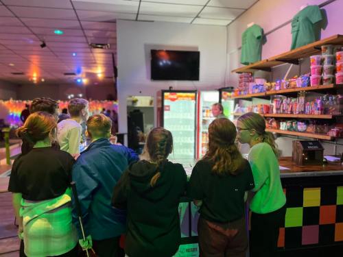 A group of children stands at a counter in a colorful arcade, looking at a vending machine and snacks on shelves.