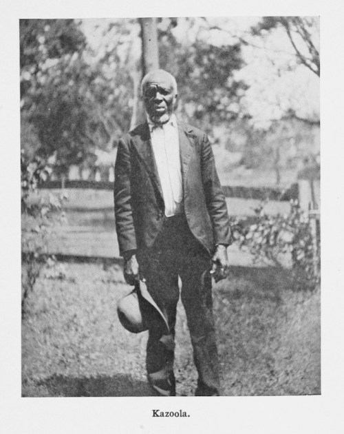 A historical black-and-white photo of an elderly man in a suit holding a hat, standing outdoors.