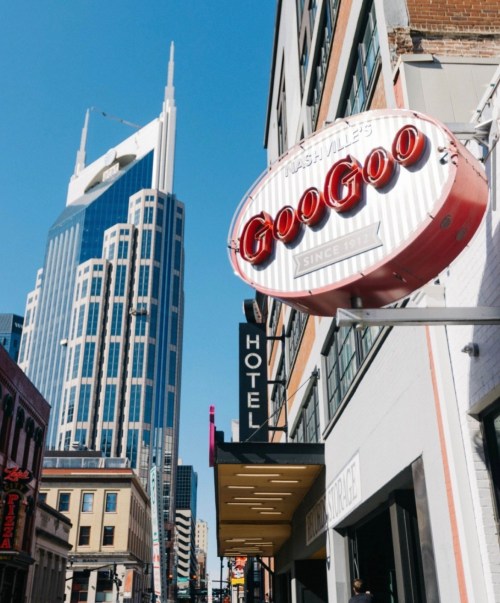 A street view featuring a retro sign for GooGoo and a tall modern building in Nashville under a clear blue sky.