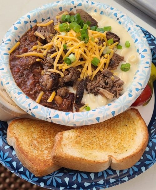 A bowl of chili topped with cheese and green onions, served with a side of toasted bread on a decorative plate.