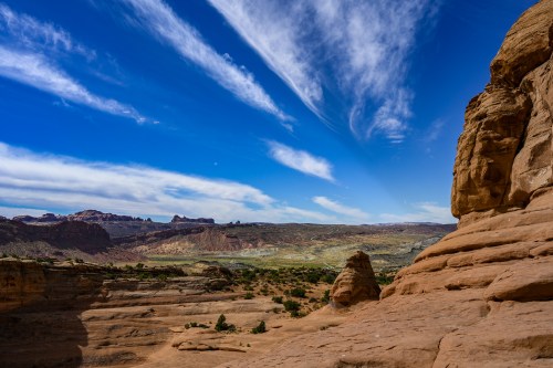 A scenic view of rocky terrain under a blue sky with wispy clouds, showcasing layered cliffs and distant hills.