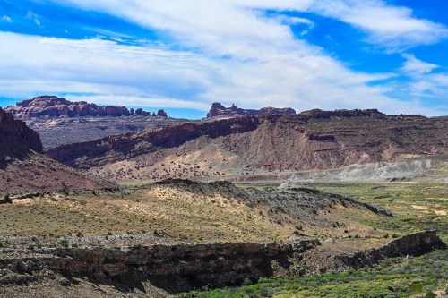 A vast landscape featuring rugged mountains, rolling hills, and a clear blue sky with scattered clouds.