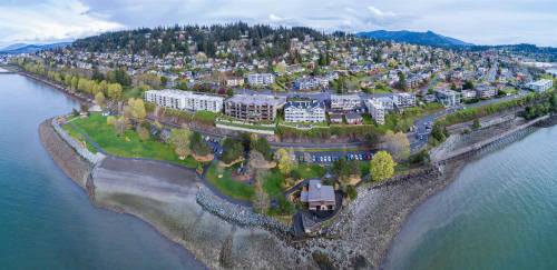 Aerial view of a coastal area with residential buildings, green parks, and a waterfront along a calm body of water.