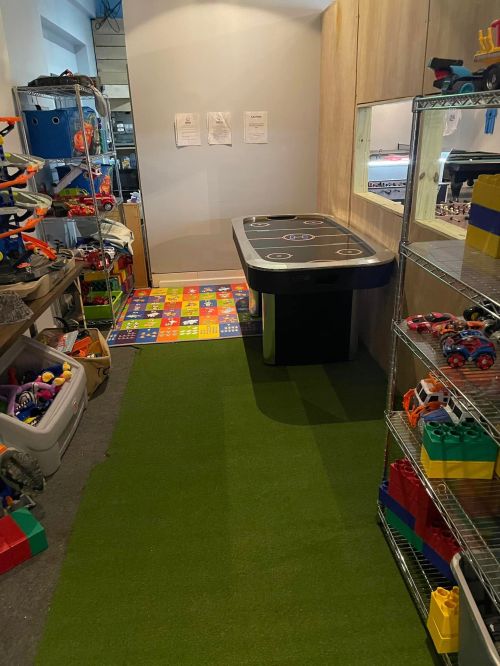 A playroom with a green carpet, shelves of toys, and an air hockey table in a well-organized space.