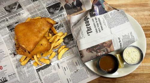 A plate of fish and chips served with two dipping sauces, placed on a table with newspaper underneath.