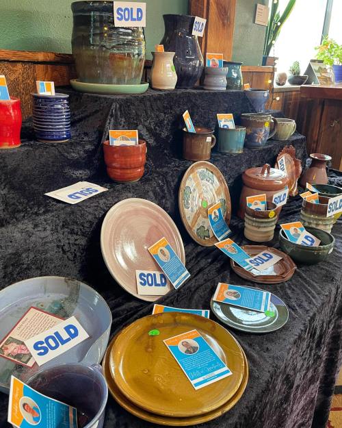 A display of various sold pottery pieces on a black tablecloth, each with a tag indicating it has been sold.