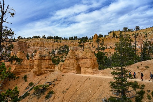 A scenic view of a canyon with unique rock formations and hikers on a trail under a cloudy sky.
