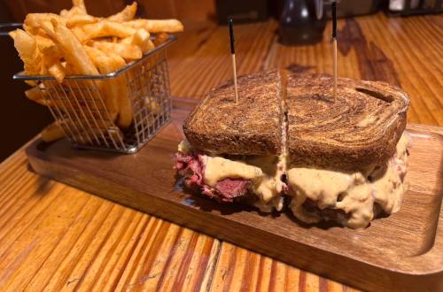 A sliced sandwich with melted cheese and meat on toasted bread, served with a side of crispy fries in a small basket.