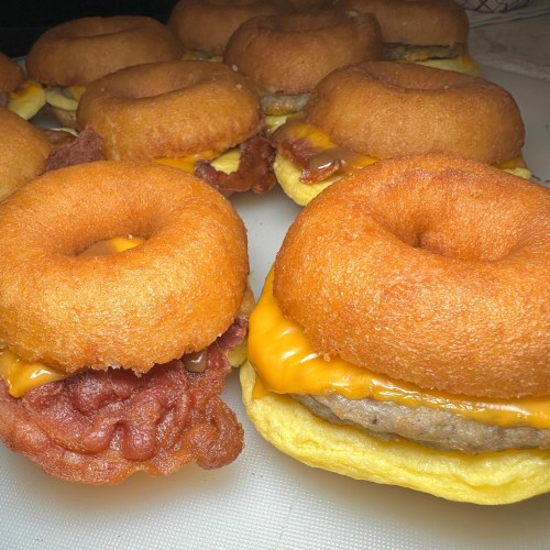 A close-up of donut sandwiches filled with bacon, sausage, and melted cheese on a white surface.