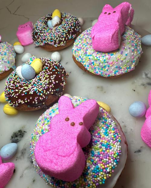 Colorful donuts topped with icing, sprinkles, and pink marshmallow bunnies, surrounded by candy eggs.