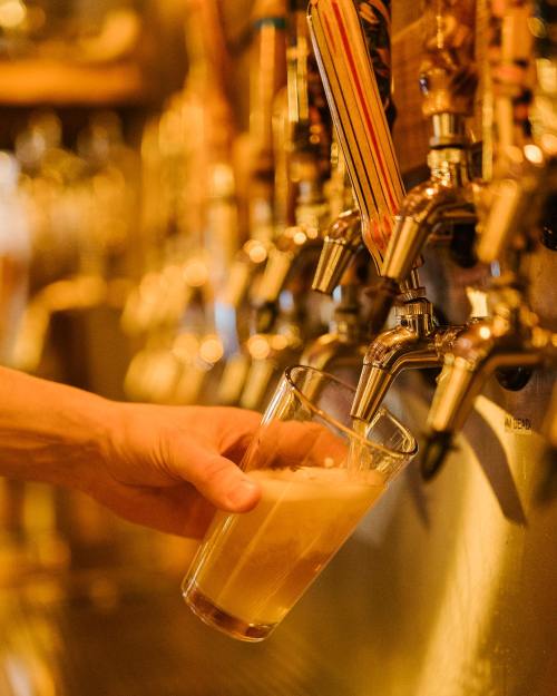 A hand pours beer from a tap into a glass at a bar, with multiple taps in the background.