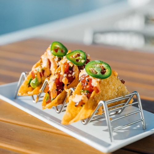 Three crispy tacos topped with jalapeños, cheese, and salsa, served on a white plate with a wooden table background.
