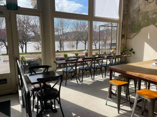 Bright café interior with wooden tables and chairs, large windows overlooking a river and trees outside.
