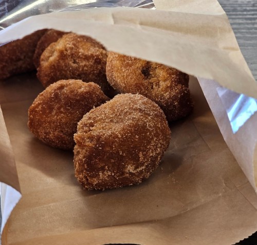 A bag containing several golden-brown, sugar-coated doughnuts on a brown paper surface.