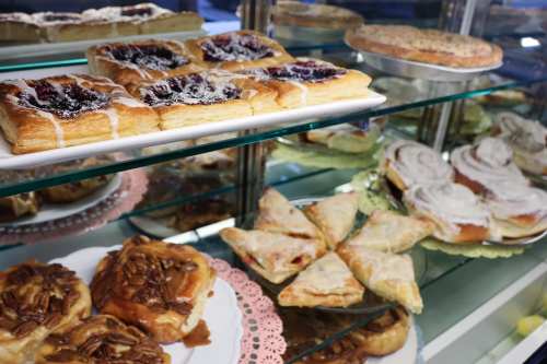 A display case filled with various pastries, including fruit danishes, cinnamon rolls, and pecan sticky buns.
